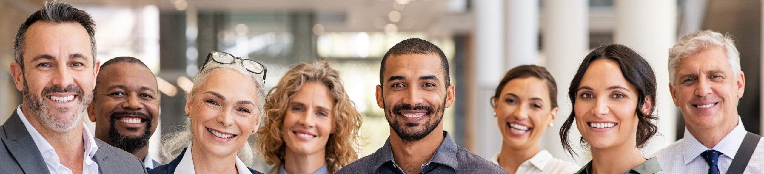 Portrait of successful group of business people at modern office looking at camera. Portrait of happy businessmen and satisfied businesswomen standing as a team. Multiethnic group of people smiling and looking at camera.
